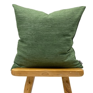 May include: A green throw pillow with a textured fabric sits on a wooden stool.