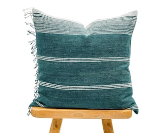 May include: Teal and white striped cushion with fringe trim, sitting on a wooden stool.