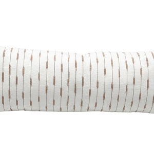 Pu&ograve; includere: Un lungo cuscino decorativo rettangolare con sfondo bianco e trattini marroni verticali. Il cuscino ha un aspetto strutturato ed &egrave; progettato per un letto o un divano.