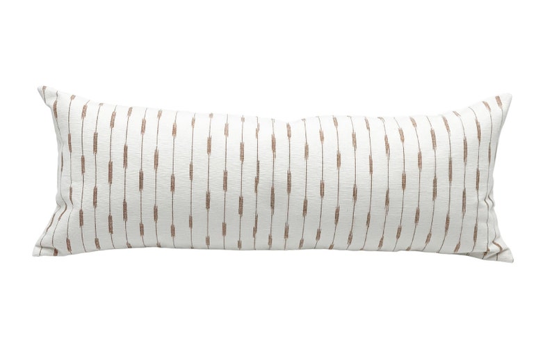 Pu&ograve; includere: Un lungo cuscino decorativo rettangolare con sfondo bianco e trattini marroni verticali. Il cuscino ha un aspetto strutturato ed &egrave; progettato per un letto o un divano.