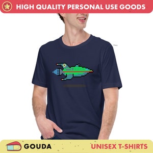 May include: A navy blue unisex t-shirt with a pixelated spaceship graphic. The spaceship is green, blue, and red. The text "GOUDA" is in the bottom left corner and "UNISEX T-SHIRTS" is in the bottom right corner.