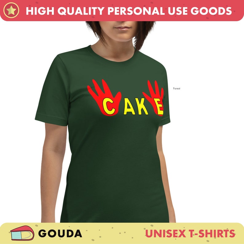 May include: A forest green unisex t-shirt featuring the word "CAKE" in yellow, with red hand graphics. The t-shirt has a crew neck and short sleeves.