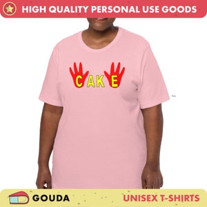 May include: Pale pink unisex t-shirt featuring the word "CAKE" in yellow letters and red hand graphics. The shirt has a crew neck and short sleeves. The text "HIGH QUALITY PERSONAL USE GOODS" is at the top.