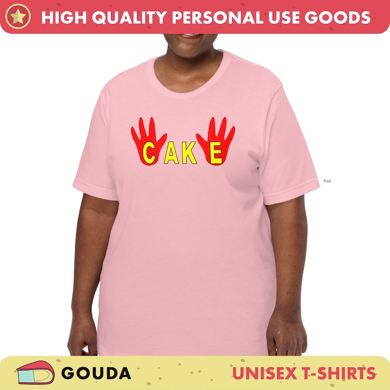May include: Pale pink unisex t-shirt featuring the word "CAKE" in yellow letters and red hand graphics. The shirt has a crew neck and short sleeves. The text "HIGH QUALITY PERSONAL USE GOODS" is at the top.