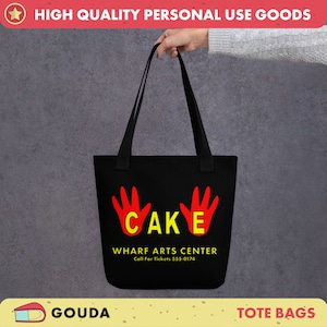 Könnte beinhalten: Schwarze Tragetasche mit roten Handabdrücken und gelber Aufschrift "CAKE" und "WHARF ARTS CENTER" mit der Telefonnummer "555-0174".