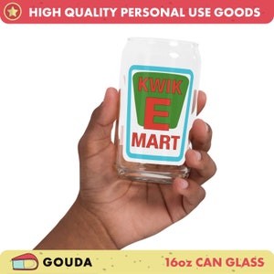 Puede incluir: Un vaso de vidrio transparente de 473 ml con forma de lata con un logotipo Kwik-E-Mart verde, rojo y azul. El vaso está siendo sostenido por una mano.