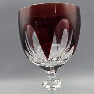 May include: A clear wine glass with a deep burgundy rim and intricate cut glass design. The glass has a faceted stem and a rounded bowl, showcasing a classic aesthetic. The glass is ideal for serving wine.