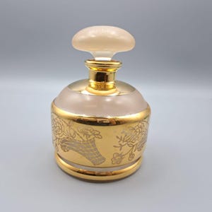 May include: A vintage perfume bottle with a gold base and accents. The bottle has a frosted glass body with a floral design and a mushroom-shaped stopper. The bottle is approximately 4 inches tall.