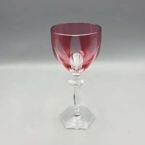 May include: A single wine glass with a ruby-coloured bowl and a clear, faceted stem. The glass has a hexagonal base and a decorative design etched into the bowl. The stem is clear and has a decorative element near the bowl.