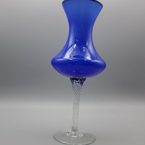 Op de afbeelding: Een kobaltblauwe glazen vaas met een bolvormig lichaam en een gedraaide steel. De vaas heeft een uitlopende bovenkant en een heldere, cirkelvormige basis. Het glas heeft een glanzende afwerking. Een decoratief item.