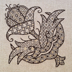 Puede incluir: Un diseño bordado en negro y dorado sobre un fondo de tela beige. El diseño presenta patrones intrincados y remolinos.