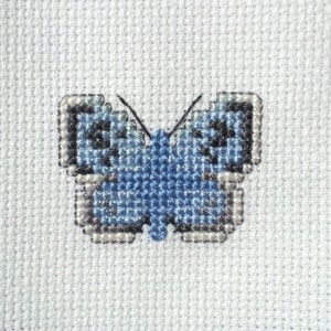 May include: A blue butterfly cross-stitch pattern on white fabric.
