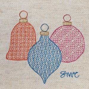 May include: Embroidered Christmas baubles in red, blue, and pink. The baubles feature a detailed, geometric pattern and gold-coloured caps. The design includes a bell-shaped bauble, a teardrop-shaped bauble, and a round bauble. The initials "smc" are embroidered in blue.