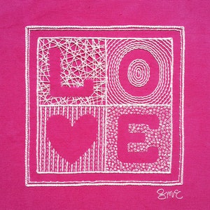 Op de afbeelding: Wit geborduurde "LOVE" op een roze stoffen achtergrond. De letters zijn gemaakt van verschillende steekpatronen.