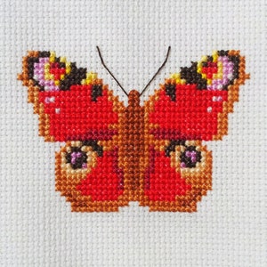 May include: A red and brown butterfly cross-stitch pattern with white accents. The butterfly is embroidered on a white fabric.