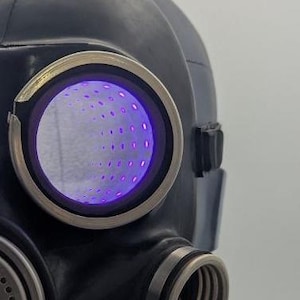 Peut inclure: Un masque à gaz noir avec une lumière LED violette dans les pièces oculaires. Le masque a un microphone argenté et un filtre noir en bas.