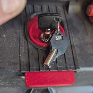 May include: Close-up of a black key with the number "001" on it, inserted into a red circular lock. The key is attached to a key ring. The lock is set in a black plastic case with a red rectangular latch.