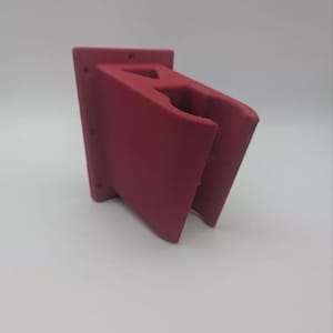 May include: A burgundy wall-mounted holder, likely for a garden hose or similar item. The holder features a rectangular back with several small holes and a curved front section. The item is made of a solid material and is designed to hold an object.