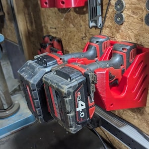 May include: Red 3D-printed power tool battery holder mounted on a wall, holding two black and red power tool batteries. The batteries are labeled M18 4.0. The holder is designed to store power tool batteries.