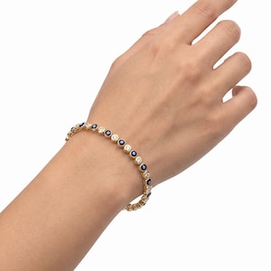 May include: A gold-toned bracelet featuring an alternating pattern of small, circular blue and white evil eye charms and clear, round-cut stones set in a continuous metal chain that wraps around the wrist with a secure clasp mechanism.