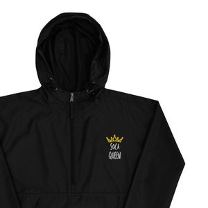 May include: Black hooded windbreaker with a gold crown and the text "Soca Queen" embroidered on the front. The jacket has a zip closure and a drawstring hood.