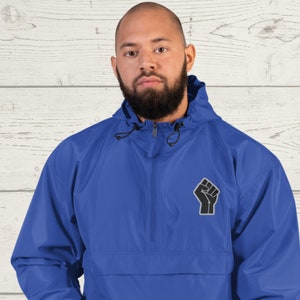 May include: A royal blue hooded jacket with a black raised fist design on the left chest. The jacket has a zipper closure and a kangaroo pocket.