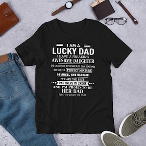 May include: Black t-shirt with white text that reads "I am a Lucky Dad. I have a freaking awesome daughter. She's stubborn, messy and a bit silly sometimes but she is a perfect mixture of angel and warrior. We are the best partners in crime and I'm proud to be her dad (yes, she bought me this)"