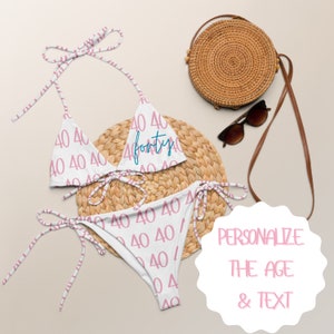 May include: White bikini with pink and white stripes. The bikini top and bottom are printed with the number "40" and the word "forty" in blue. The bikini is on a woven straw mat. The text "PERSONALIZE THE AGE & TEXT" is on a white circle.