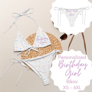 May include: White bikini with a confetti pattern and the text "Birthday Girl" in purple. The bikini is shown on a straw mat with sunglasses and a brown strap.