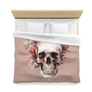 Könnte beinhalten: Eine Aquarell-Illustration eines menschlichen Schädels mit rosa und roten Blumen. Der Schädel ist weiß mit schwarzen Augenhöhlen und einem zahnigen Grinsen. Der Hintergrund ist hellbraun.