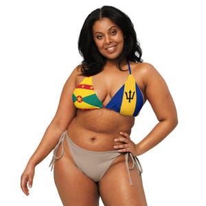 May include: A two-piece bikini set featuring a triangle top and a low-rise bottom. The top displays the flags of Grenada and Barbados. The bikini bottom is a solid taupe color. The woman is smiling and posing.