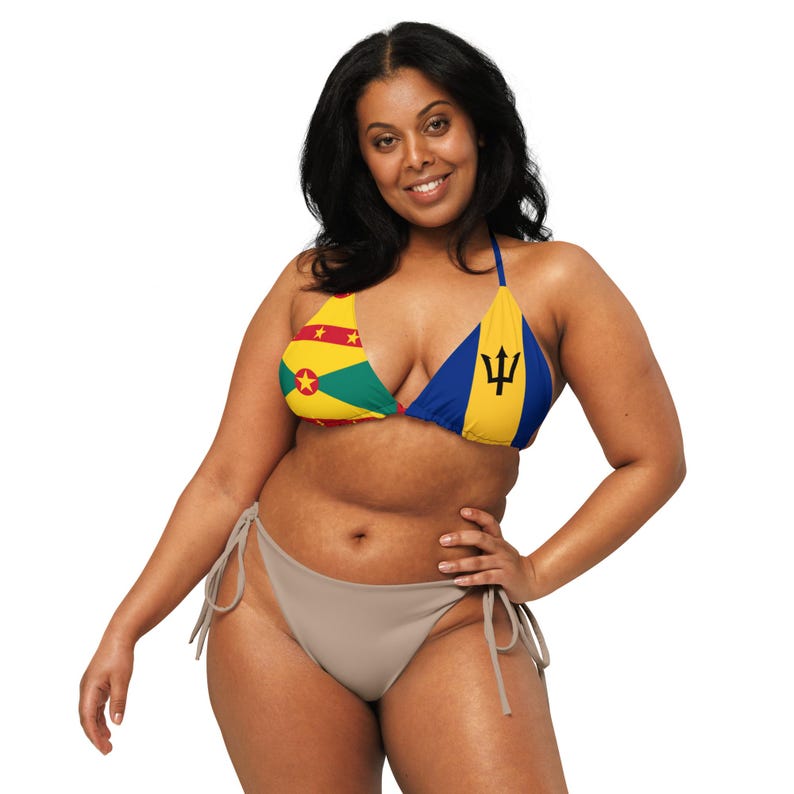 May include: A two-piece bikini set featuring a triangle top and a low-rise bottom. The top displays the flags of Grenada and Barbados. The bikini bottom is a solid taupe color. The woman is smiling and posing.