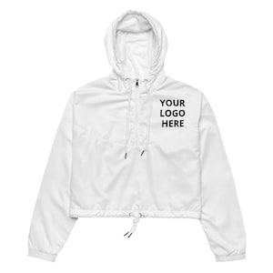 Könnte beinhalten: Weiße, kurze Kapuzenjacke mit Kordelzug am Saum und Reißverschluss. Die Jacke hat einen schwarzen Textaufdruck mit der Aufschrift "YOUR LOGO HERE".