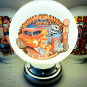 Puede incluir: Una luz de gasolinera blanca en forma de globo con un gráfico rojo, blanco y azul de un coche de carreras vintage y una chica pin-up. El gráfico incluye el texto "Reliable Service Trixie's Road Service 1-555 TRI-XIES Established 1947 Road Girl Garage".