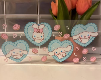 Può includere: Foglio di adesivi trasparente con personaggi dei cartoni animati in cornici a forma di cuore azzurro. Il foglio include immagini di un personaggio coniglio, cuori rosa e disegni a spirale rosa. Un vaso di tulipani arancioni è sullo sfondo.