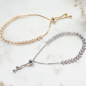 Peut inclure: Deux bracelets réglables présentant un motif de feuilles délicat sur la chaîne. Un bracelet est fini dans un ton doré brillant, tandis que l'autre est fini dans un ton argenté. Chaque pièce comprend un mécanisme à perle coulissante pour le réglage.