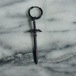 May include: Black sword-shaped earring with a hoop design. The sword has a winged design at the top and a pointed tip.