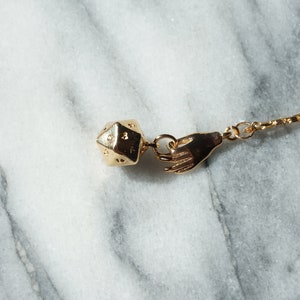 May include: A gold chain necklace with a gold hand charm and a gold dice charm.