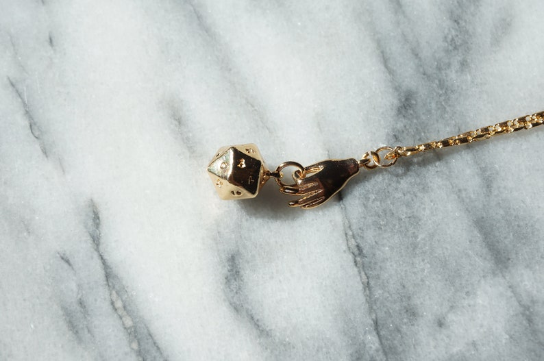 May include: A gold chain necklace with a gold hand charm and a gold dice charm.
