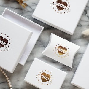 May include: Five white boxes with gold foil logos of a heart with the text "MCCCHANG" inside. The boxes are on a marble surface.