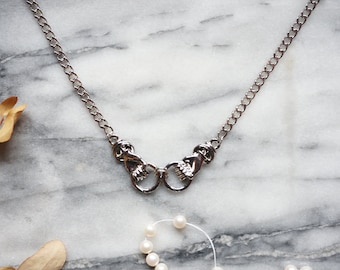 May include: A silver chain necklace with two clasped hands as the pendant.