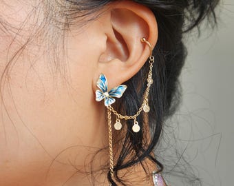 Op de afbeelding: Gouden vlinder oorcuff met een hangende blauwe kristallen hanger en een ketting met kleine gouden schijven.