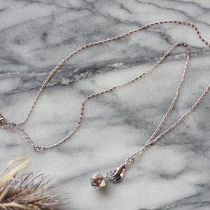 May include: A silver chain necklace with a small silver charm hanging from it. The charm is a cube with a hand holding a star on top.