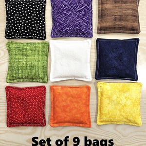 May include: Nine square fabric bags in various colors and patterns, including black with white polka dots, purple with small white dots, and brown with a wood grain design. The text "Set of 9 bags" is at the bottom.