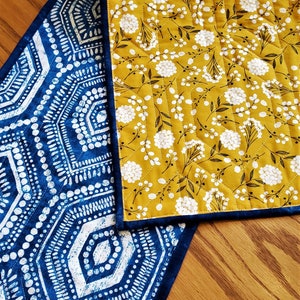 May include: A blue and white geometric patterned table runner with a yellow floral patterned fabric on the back side.
