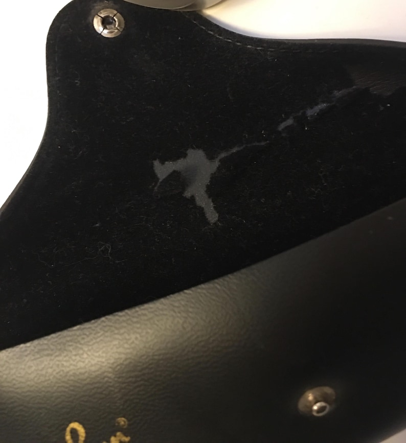 May include: Black eyeglass case with a snap closure. The interior is lined with black velvet, showing a stain. The exterior is smooth black leather. The case is open, revealing the interior.