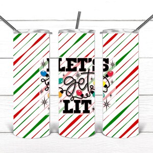 May include: A set of three stainless steel tumblers with lids and straws. The tumblers have a white background with red and green diagonal stripes. The center tumbler has the text "LET'S get LIT" with Christmas lights.