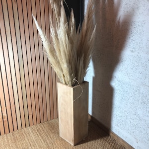 Peut inclure: Un vase en bois rectangulaire et haut avec une finition en bois naturel. Le vase est rempli d'herbe de pampa séchée, un choix populaire pour la décoration intérieure moderne.