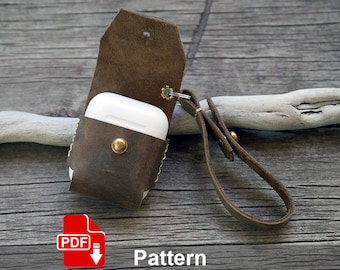 May include: A brown leather case with a snap closure for an AirPod case. The case has a leather strap with a metal ring. The case is sitting on a wooden surface. The text "PDF Pattern" is visible below the case.