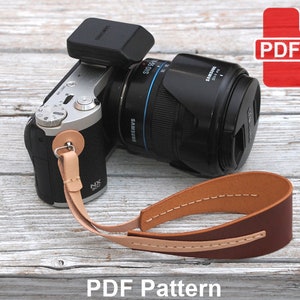 May include: A brown leather camera strap with white stitching. The strap is attached to a silver and black camera with a lens. The image includes the text "PDF Pattern".
